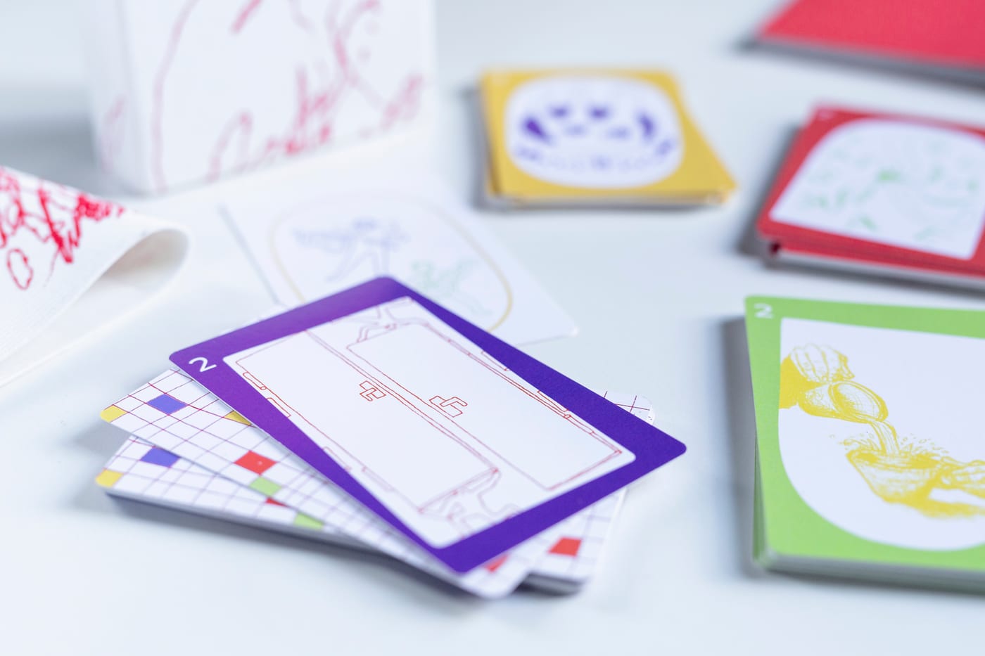 Close up: a purple two with a red line drawing of a building, card backs in a grid of coloured squares, a green two with a yellow drawing.