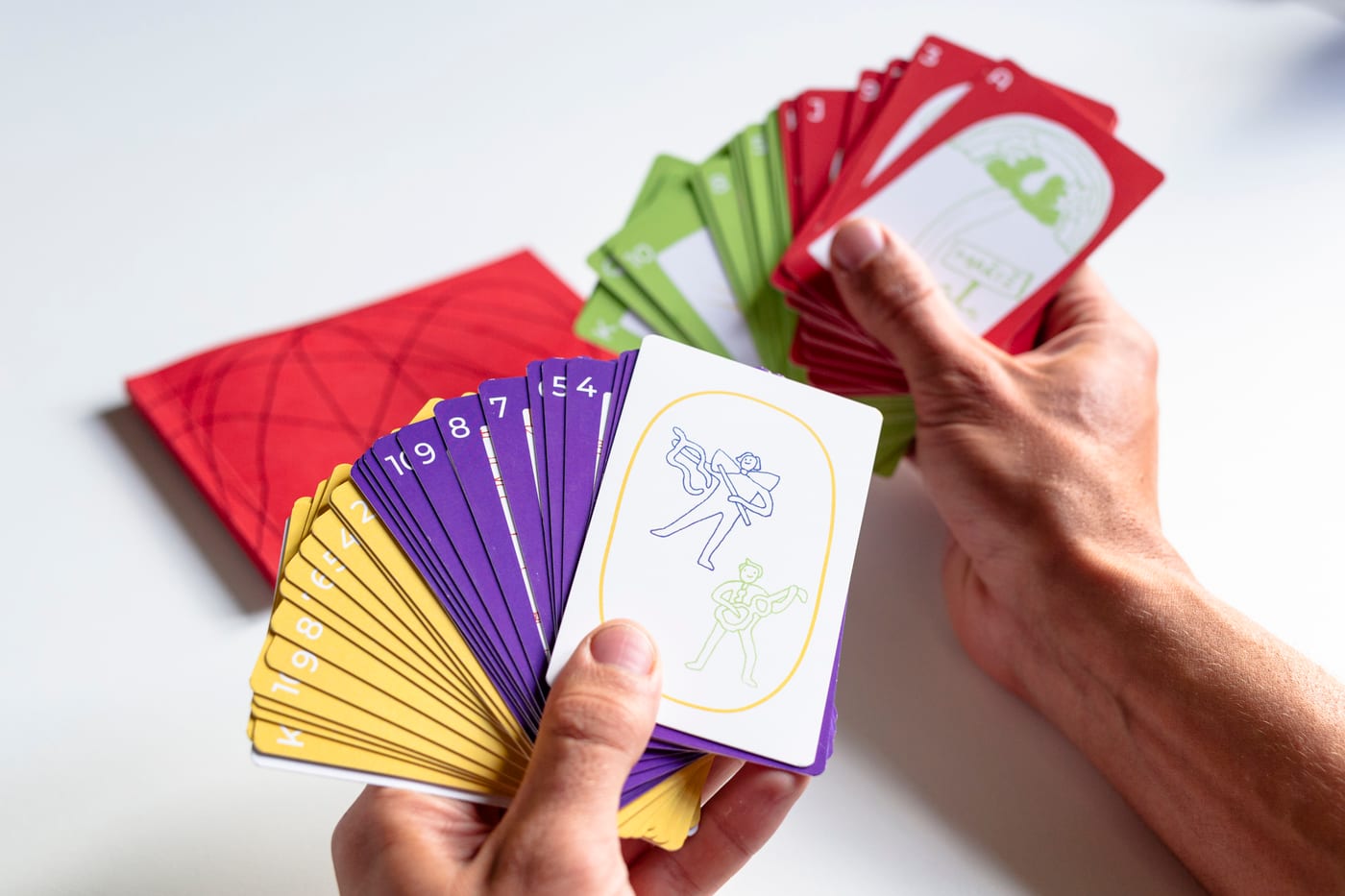 A hand fans a deck of yellow, purple, green and red cards over the red book.