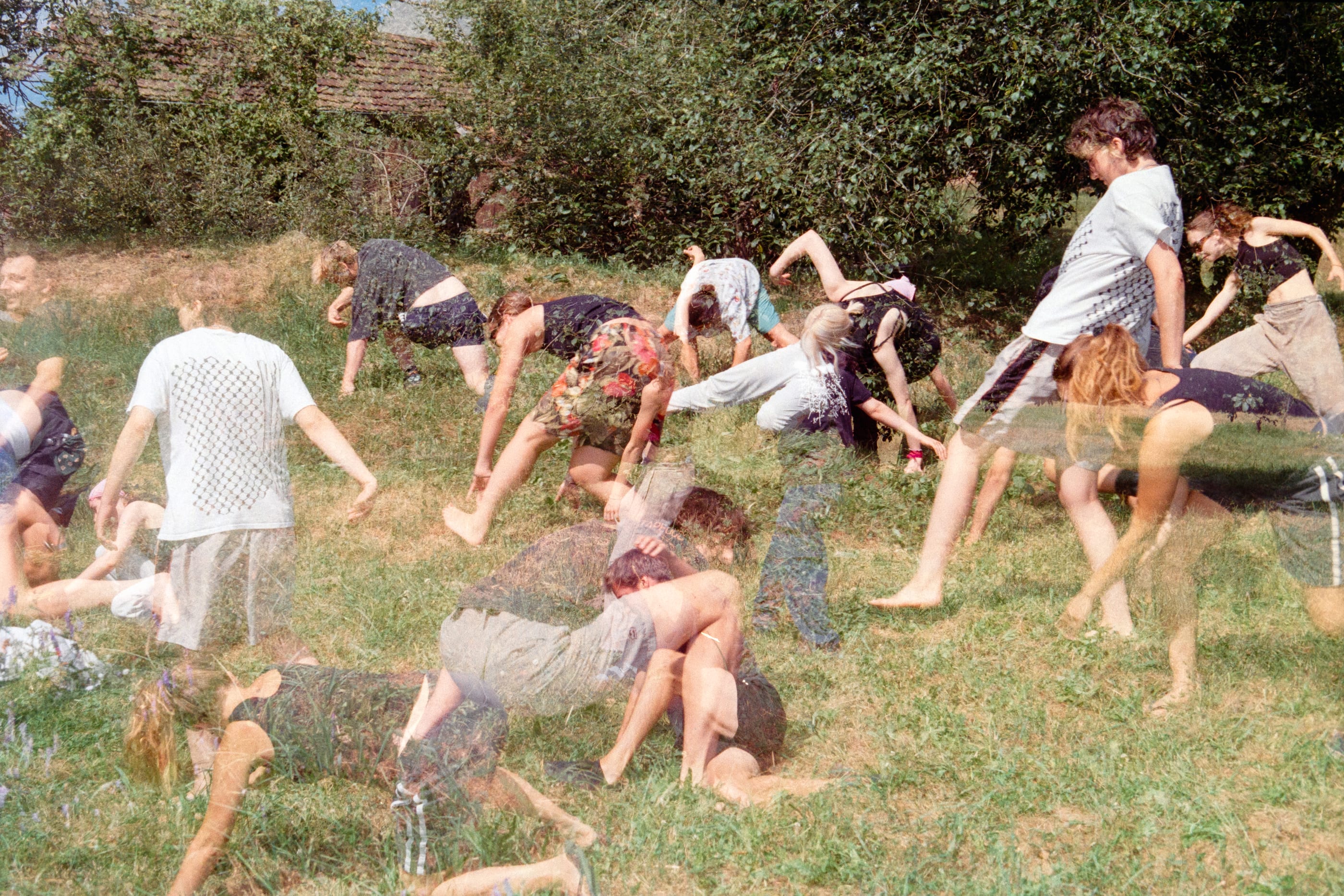 A group movement exercise on grass: barefoot people bend and turn, blurred by their motion.