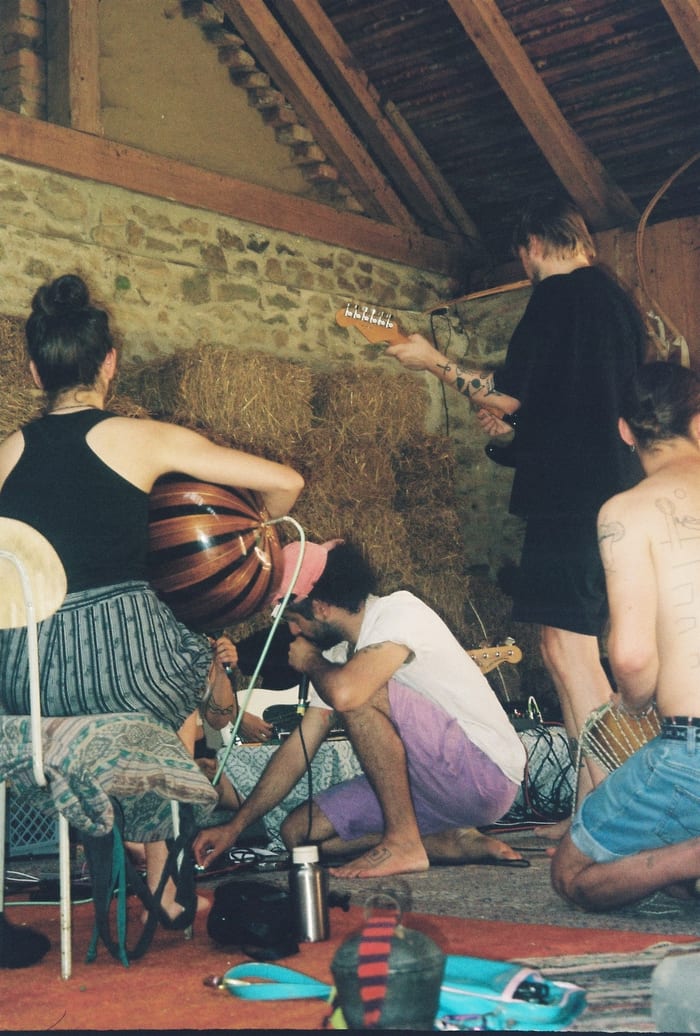 Close up in the barn: a woman holds a large striped gourd to a microphone, a man kneels with a microphone, another plays a bass.