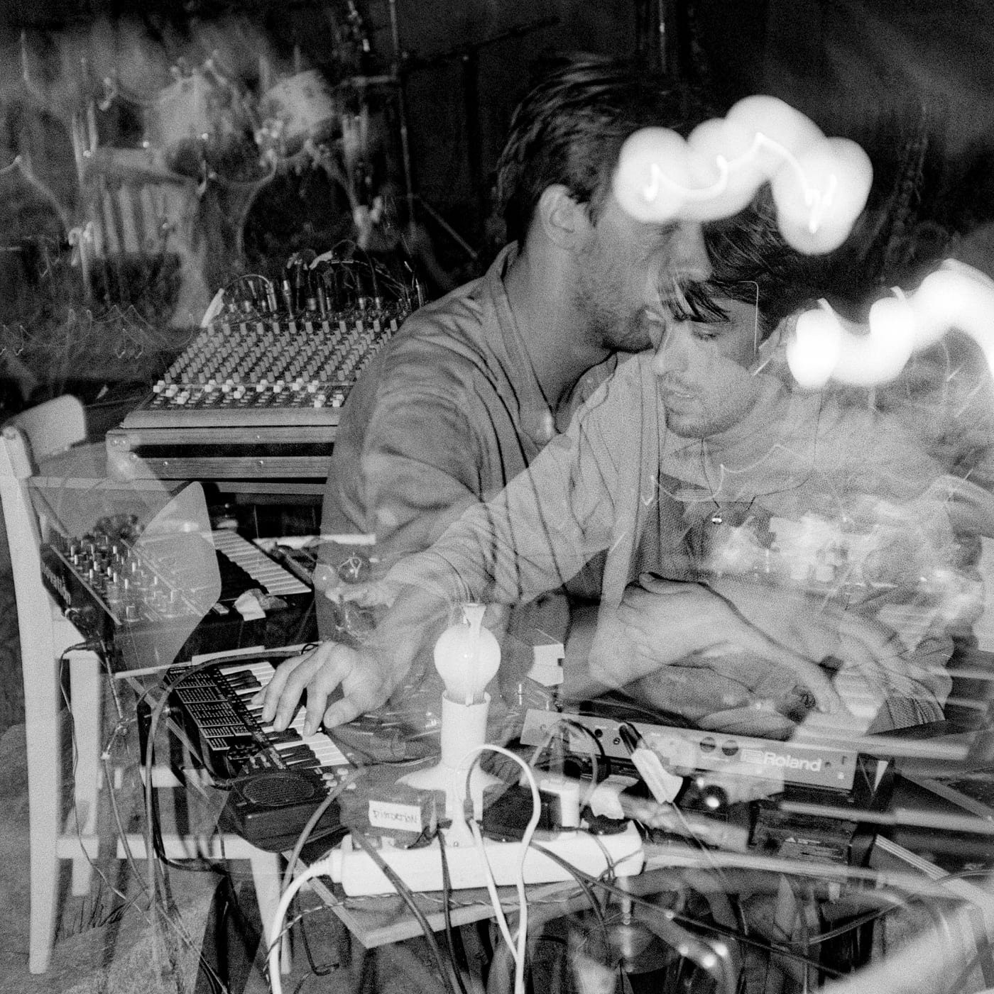 Two people at a mixing desk and keyboards, in a black and white double exposure.