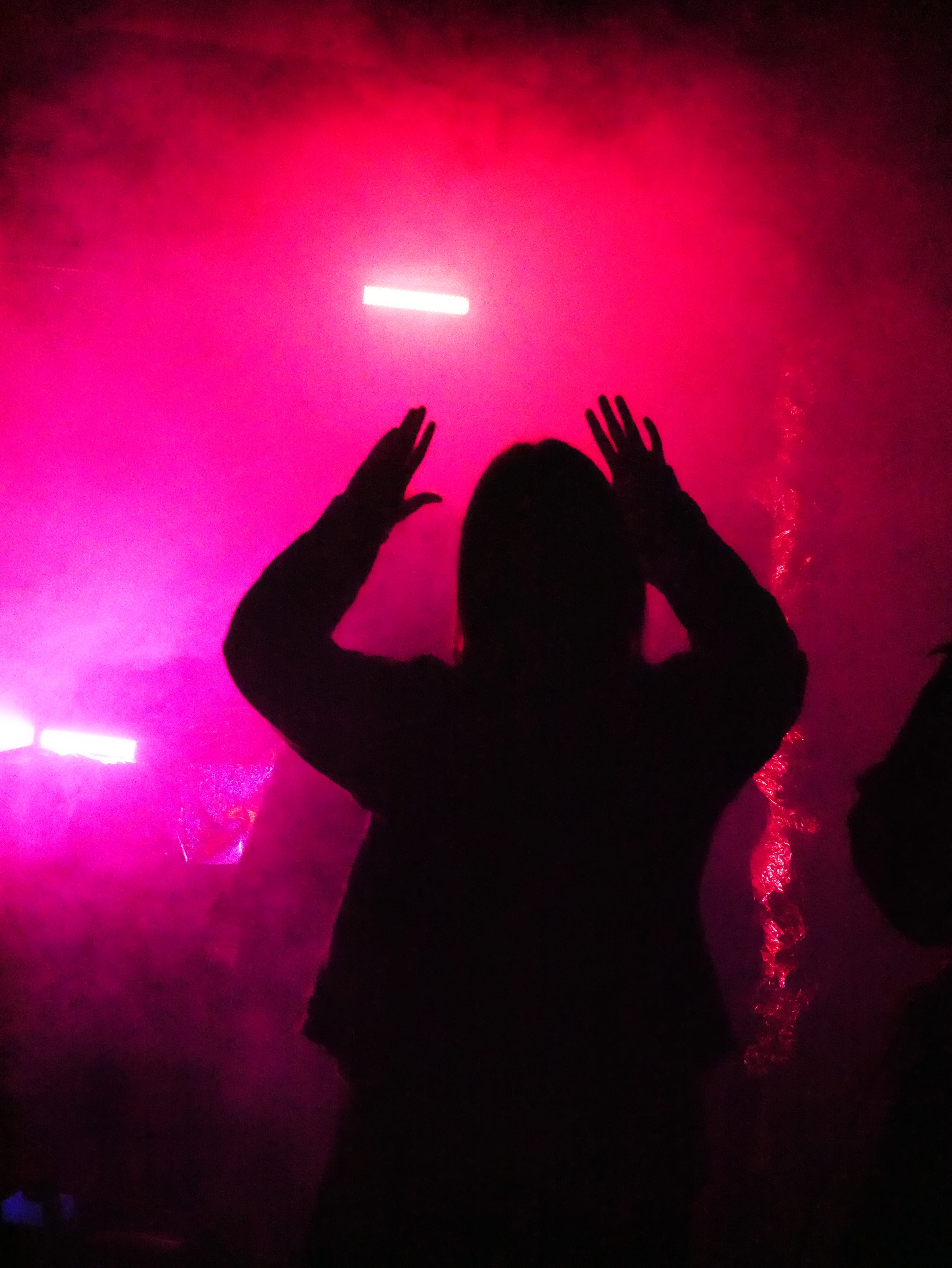 A silhouette with both hands raised against pink light and smoke.