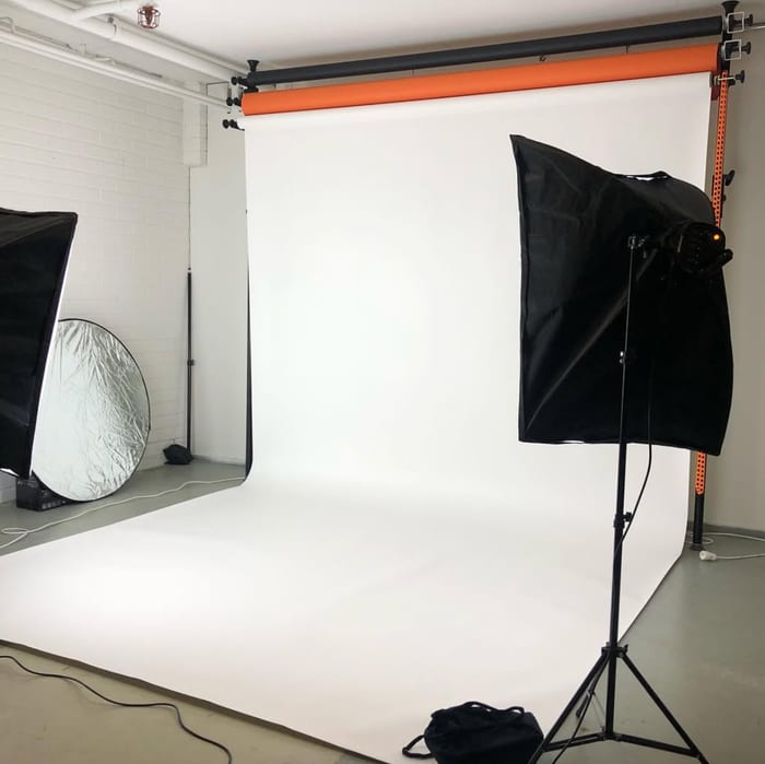A white paper backdrop rolled down from the wall onto the floor, with two softboxes and a round reflector.