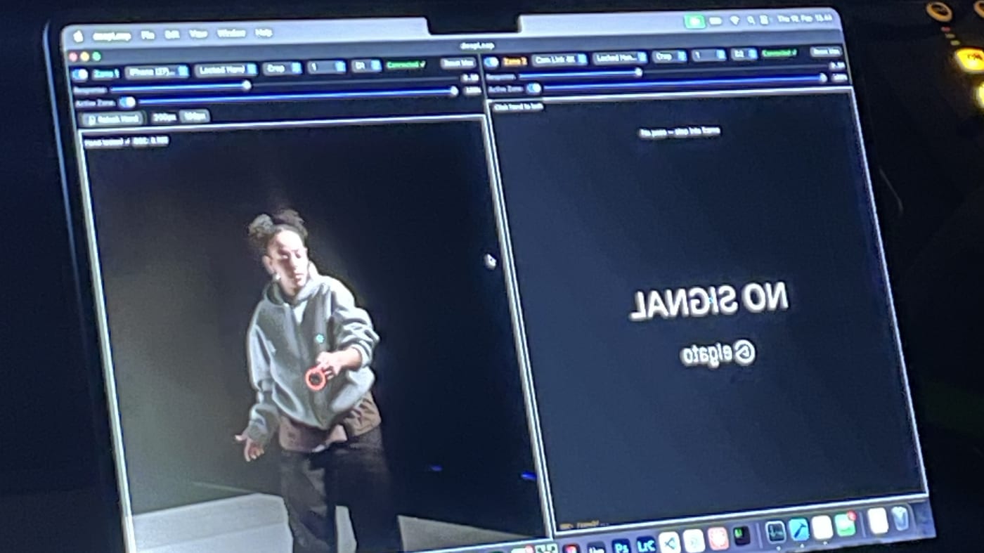 A laptop screen in a dark room. The app's window is split in two. On the left a dancer in a grey hoodie with a red ring around one hand, and rows of small controls above. On the right a mirrored no signal card from a capture device.